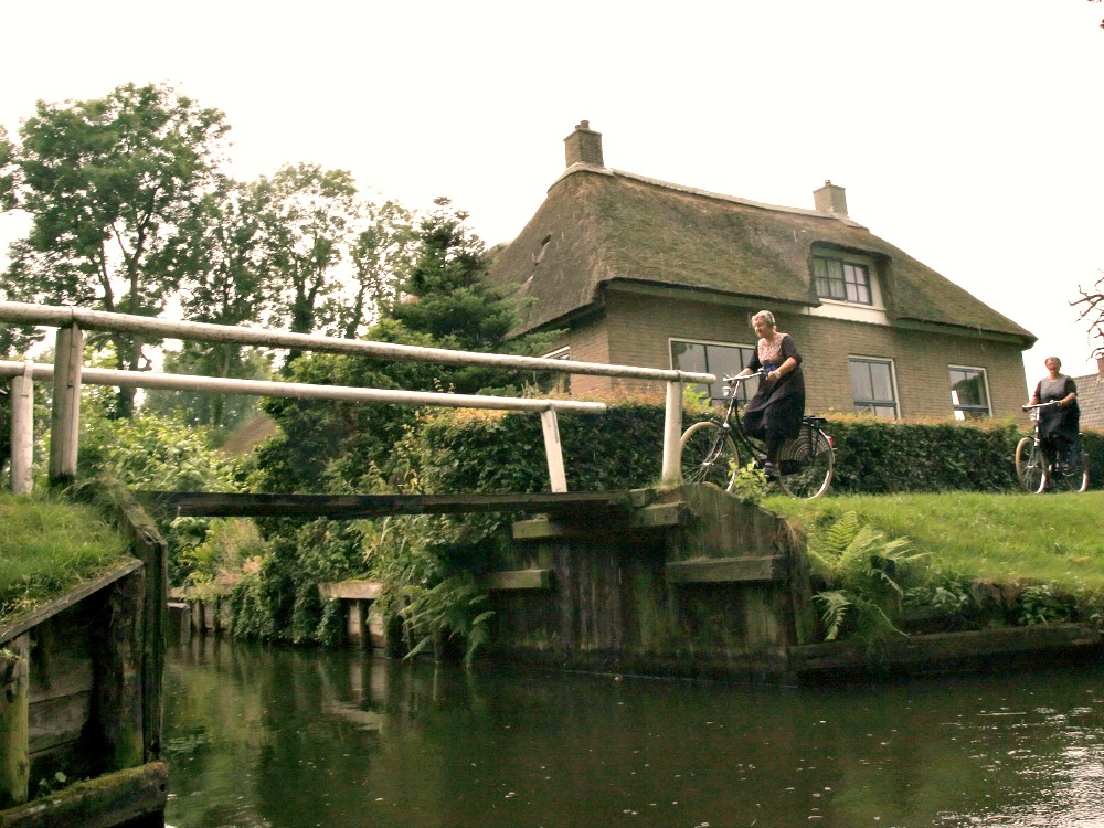 Women in traditional Dutch dress are cycling in Giethoorn